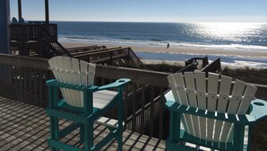 Une terrasse en bois avec deux fauteuils Adirondack donnant sur une plage.