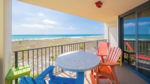 Ein Balkon mit Tisch und Stühlen, der Blick auf einen Strand mit blauem Himmel bietet.