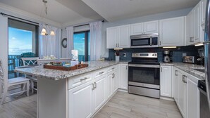 Una cocina moderna con gabinetes blancos, encimeras de granito, electrodomésticos de acero inoxidable y una isla grande con horno integrado.