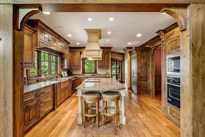 A spacious kitchen with wooden cabinets, a large island with stools, and built-in appliances.