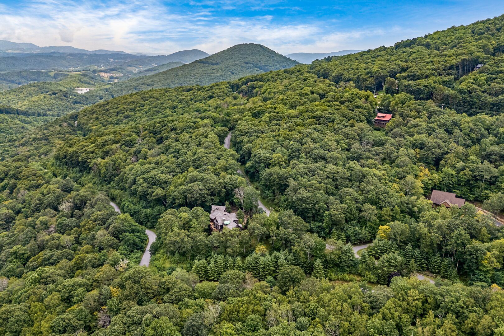 A remote cabin nestled in a dense forest with a winding road leading to it.