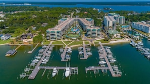 An aerial view of a marina with multiple docks and boats, surrounded by lush greenery and a large hotel complex with multiple buildings.