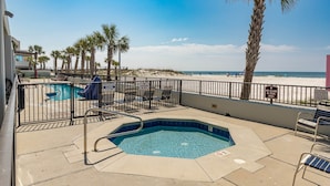 A pool area with a hot tub, lounge chairs, and a view of the beach.