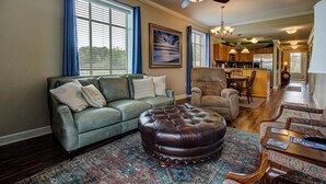 A living room with a sofa, ottoman, patterned rug, and a dining area with a table and chairs.