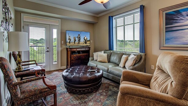 A living room with a sofa, ottoman, armchair, and a television on a stand.