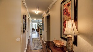 A hallway with a wooden floor, a rug, a lamp, a basket, and framed artwork on the walls.