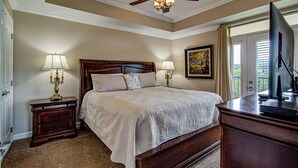 A bedroom with a large bed, two bedside tables with lamps, a dresser, a ceiling fan, and a painting on the wall.
