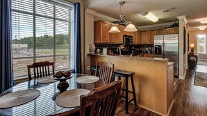 A modern kitchen with wooden cabinets, a stainless steel refrigerator, and a dining area with a glass table and chairs.