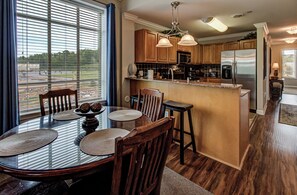 A modern kitchen with wooden cabinets, a stainless steel refrigerator, and a dining area with a glass table and chairs.