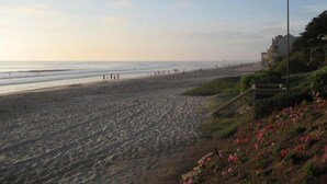 A beach with a clear sky, a few people walking, and a building on the right. - 5 Star, Large, Luxury Condo in Carlsbad Village (Carlsbad)
