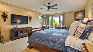 A bedroom with a large bed, a ceiling fan, a TV, and a stone accent wall. - 5 Star, Large, Luxury Condo in Carlsbad Village (Carlsbad)