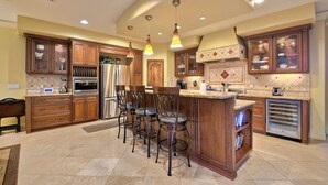 A spacious kitchen with wooden cabinets, a central island with bar stools, and pendant lighting. - 5 Star, Large, Luxury Condo in Carlsbad Village (Carlsbad)