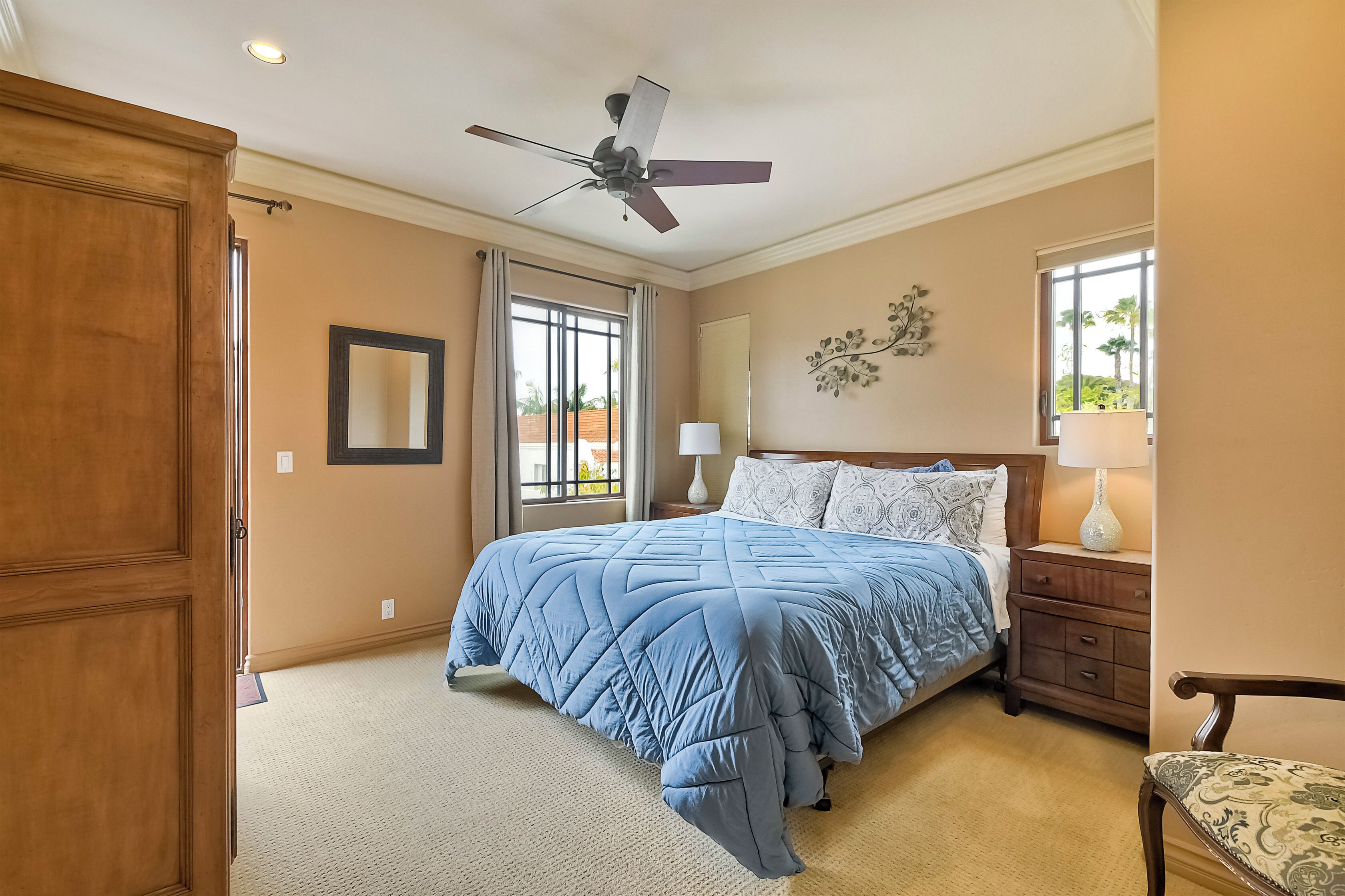 A bedroom with a bed, a nightstand, a chair, a ceiling fan, and a window.