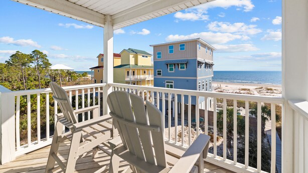 A covered balcony with two Adirondack chairs, overlooking a beach with buildings in the background. - About Time: Beach Views, Private Pool, Pet-Friendly, Dog Run and Sleeps 14 (Port St. Joe)