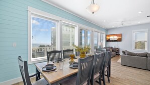 A dining area with a wooden table, chairs, and a TV mounted on the wall. - About Time: Beach Views, Private Pool, Pet-Friendly, Dog Run and Sleeps 14 (Port St. Joe)