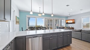 A modern kitchen with a large island, dark cabinetry, stainless steel appliances, pendant lighting, and a view to the outdoors. - About Time: Beach Views, Private Pool, Pet-Friendly, Dog Run and Sleeps 14 (Port St. Joe)