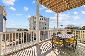 A wooden deck with a table and chairs, overlooking a beach and a building.