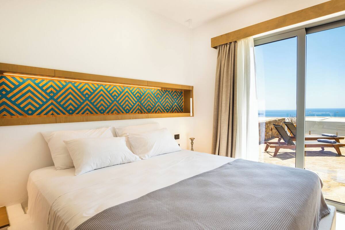 A hotel room with a large bed, a view of the beach, and a patterned wall design.