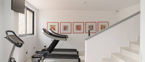 A home gym with a treadmill and stationary bike, a staircase, and framed artwork on the wall.