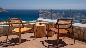 Zwei Holzstühle mit gewobenen Sitzflächen und Rückenlehnen, ein kleiner Holztisch und Blick auf das Meer und die Ferne.