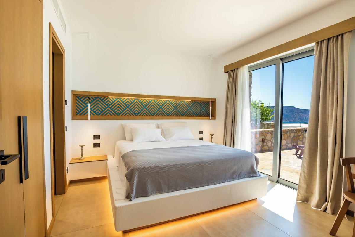 A modern bedroom with a large bed, a view of the outdoors, and a patterned wall above the bed.