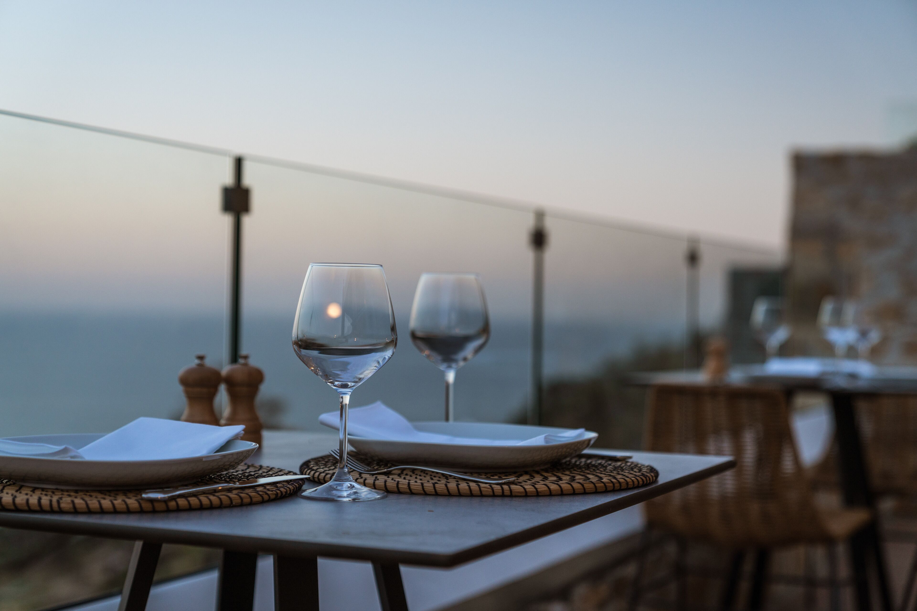 A table set for two with wine glasses and plates, overlooking a scenic view.