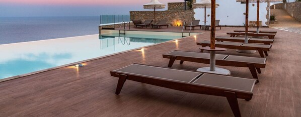 A poolside area with lounge chairs and umbrellas, overlooking the sea. - Sophid Wellness Suites Karpathos (Karpathos)