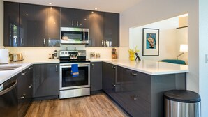 Une cuisine moderne avec des meubles de couleur sombre, des appareils en acier inoxydable et un plan de travail blanc.