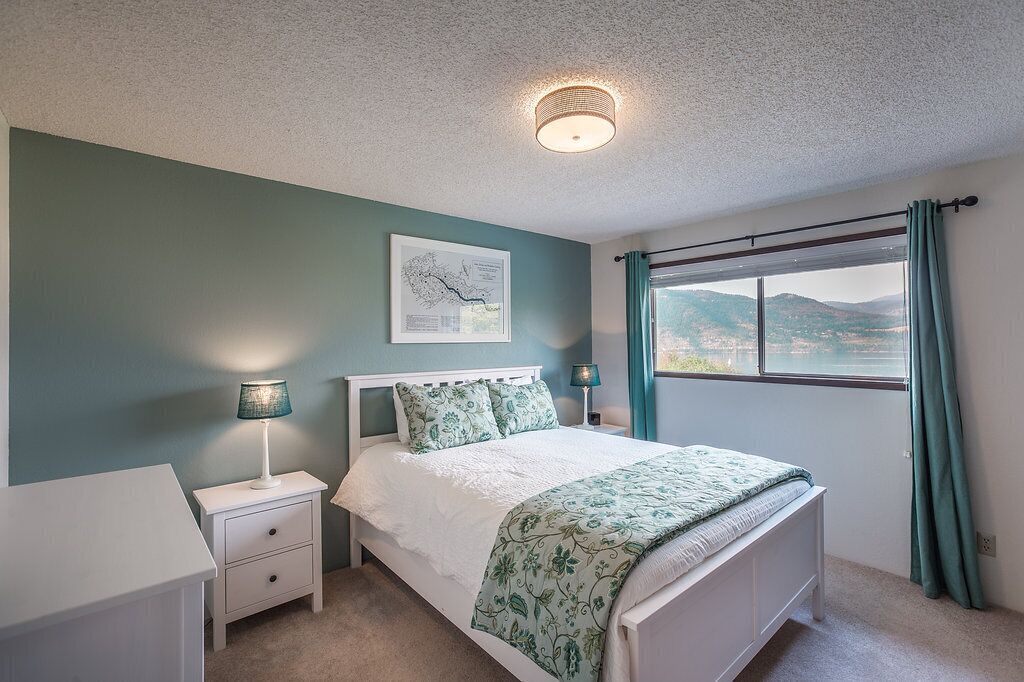 A bedroom with a bed, nightstands, a lamp, a window with curtains, and a wall-mounted light fixture.