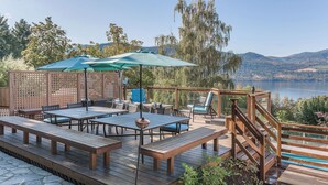 Une terrasse extérieure avec des tables et des bancs en bois, une piscine et une vue sur un lac et des montagnes.
