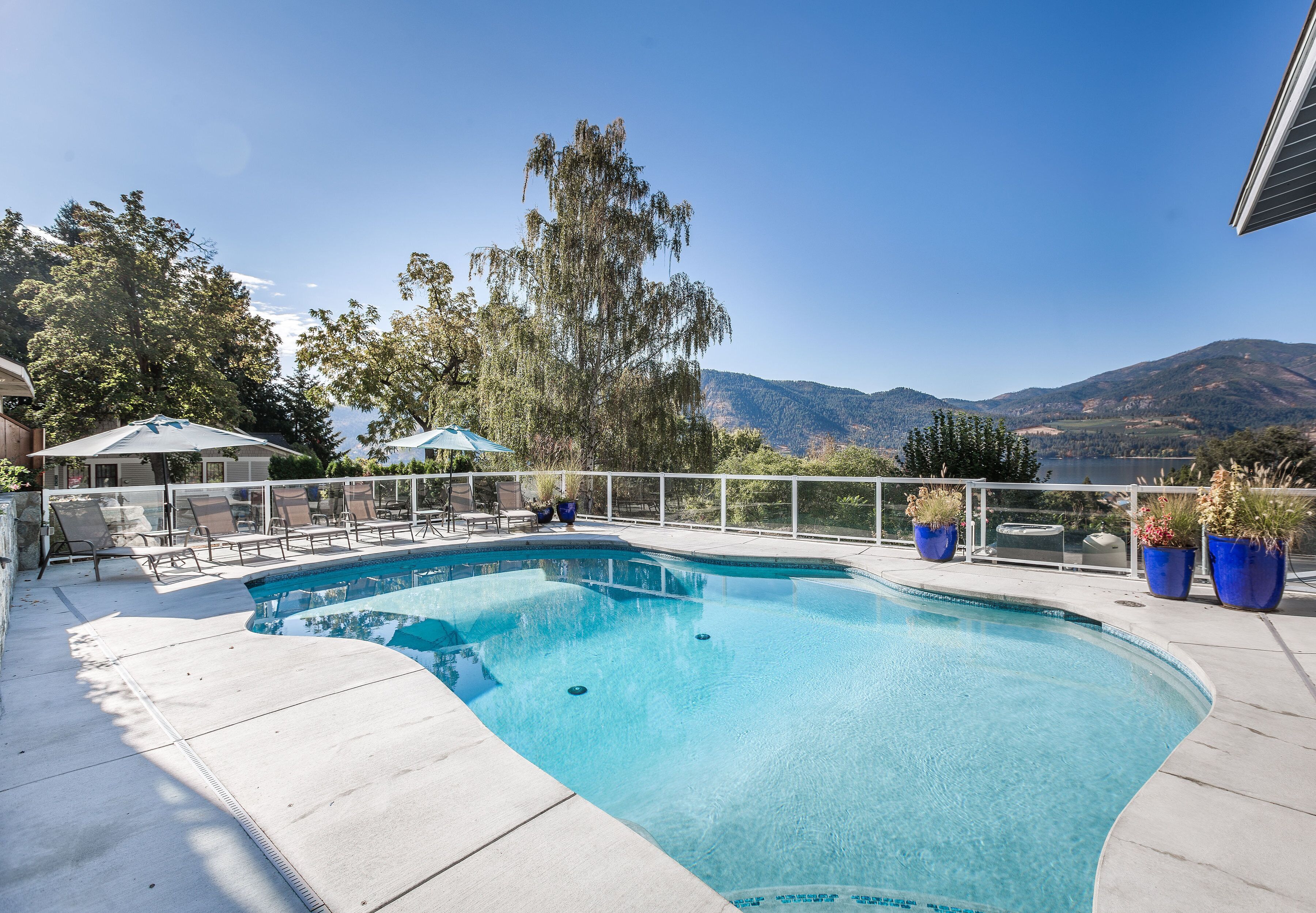 Une piscine avec vue sur les montagnes, entourée de chaises longues et de plantes en pot.