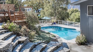 Une piscine avec des marches en pierre menant à l’eau, entourée de verdure et dotée d’une terrasse en bois.