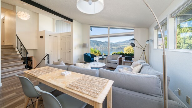 Un salon moderne avec une table à manger en bois, des canapés gris et une grande fenêtre donnant sur une vue imprenable sur les montagnes.