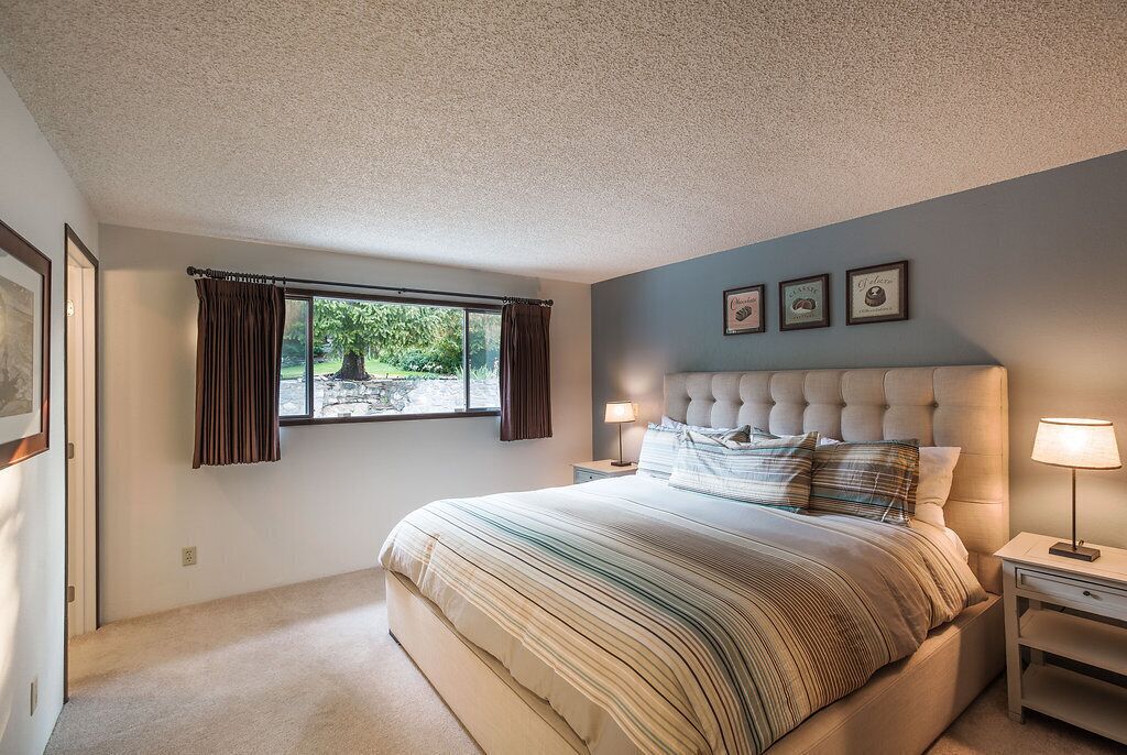 A bedroom with a large bed, two bedside tables, a window with curtains, and framed pictures on the wall.
