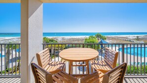 A wooden table and chairs on a balcony overlooking a beach and a pool.