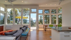 Eine moderne Küche mit großen Fenstern, einem Essbereich und einem Wohnbereich mit Sofa und Fernseher.