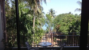 Un balcón con mesa y sillas, con vista a un jardín tropical con palmeras.