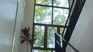 Una escalera con barandilla negra conduce a una plataforma. Se observa un ventanal con vistas a árboles.