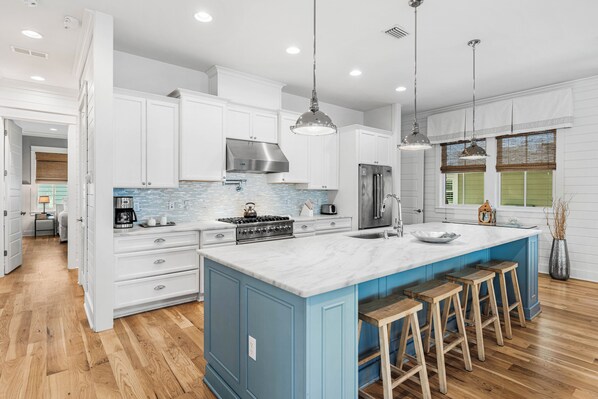 A modern kitchen with white cabinets, a blue island, wooden stools, stainless steel appliances, and pendant lighting. - Stunning WaterColor Retreat: Bikes, WaterColor Beach Club Access, Carriage House, Pure Relaxation! (Santa Rosa Beach)