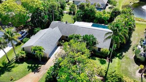 Um imóvel residencial com uma casa grande, piscina e vegetação exuberante.