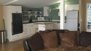 A modern living room with a sectional sofa, a dining area, and a kitchen with white cabinets and a microwave. - Pelican condo in Chimney Creek (Tybee Island)