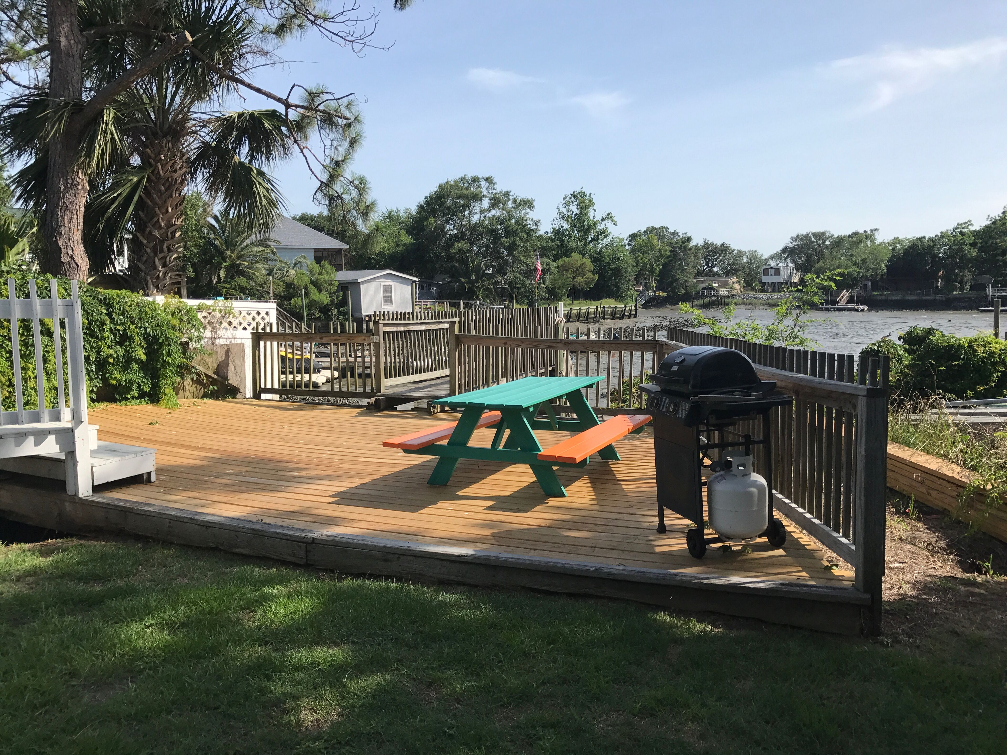 A wooden deck with picnic tables and a grill, overlooking a body of water.