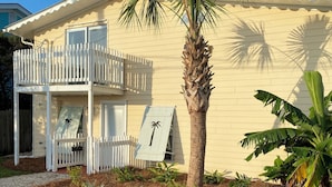 A two-story house with a balcony, a palm tree, and a garden with various plants. - Pelican condo in Chimney Creek (Tybee Island)