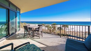Un balcon avec une table et des chaises, donnant sur une plage et l’océan.