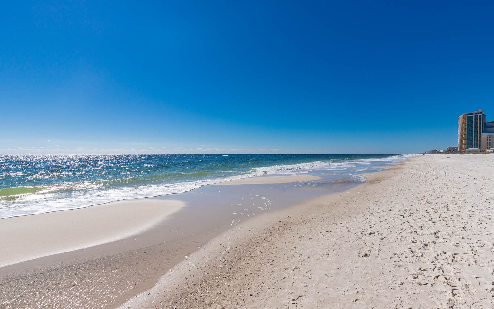 Una playa con cielo despejado, una orilla arenosa y un edificio al fondo.