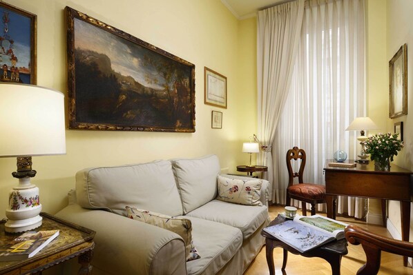 A living room with a beige sofa, a table with a lamp, a painting, and a chair.