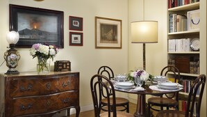 A dining area with a wooden table set for four, surrounded by wicker chairs. A bookshelf with books and decorative items is to the right. - Close to Navona Square, Exclusive cozy Apt AC, WiFi. Perfect base for touring (Roma)