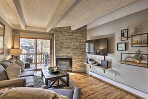 Ein modernes Wohnzimmer mit Kamin aus Naturstein, einem flachbildfernseher an der Wand und einer gemütlichen Sitzecke mit Sofa und Couchtisch.