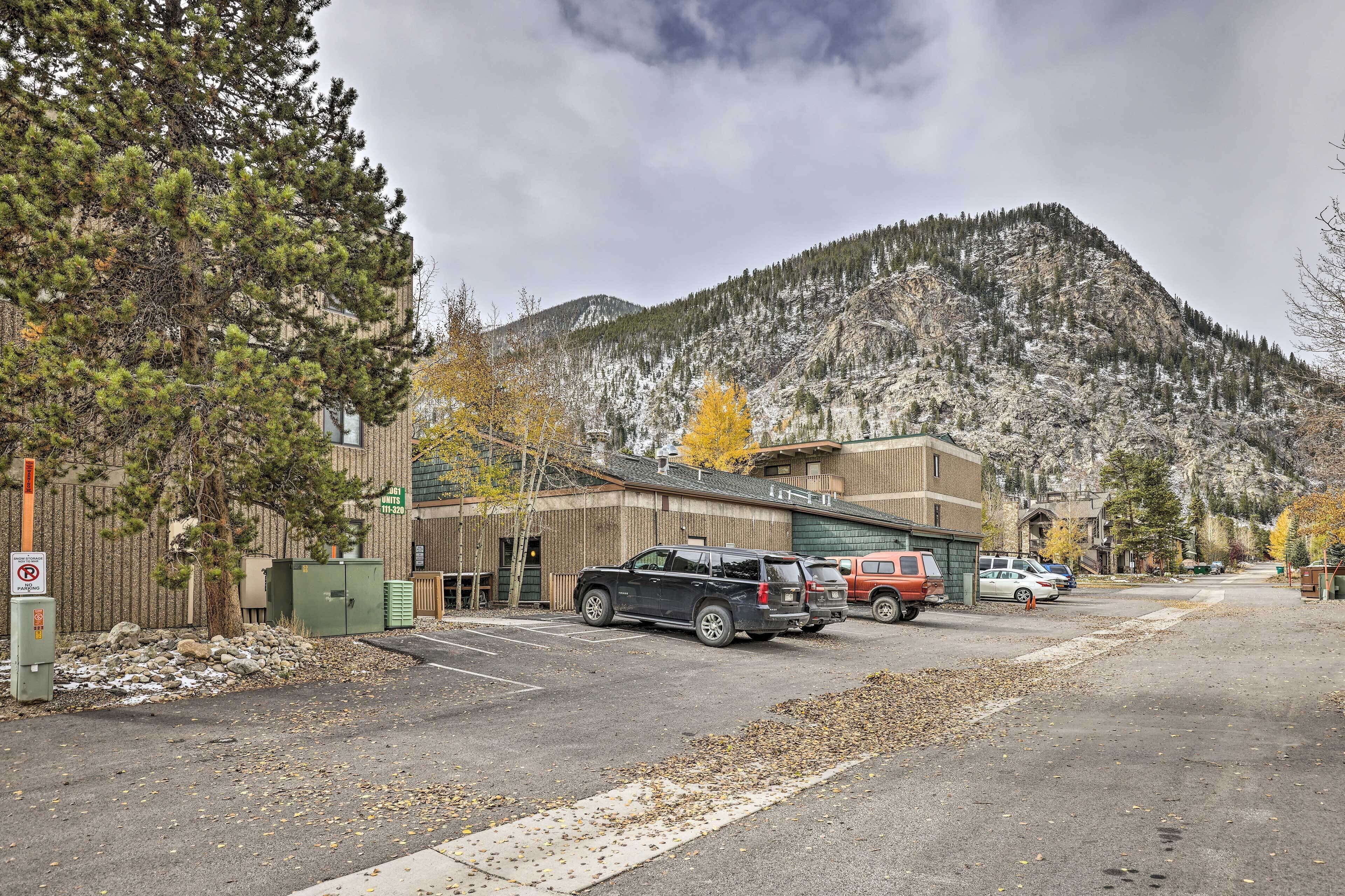 A parking lot with several cars, a building with a green roof, and a mountain in the background.