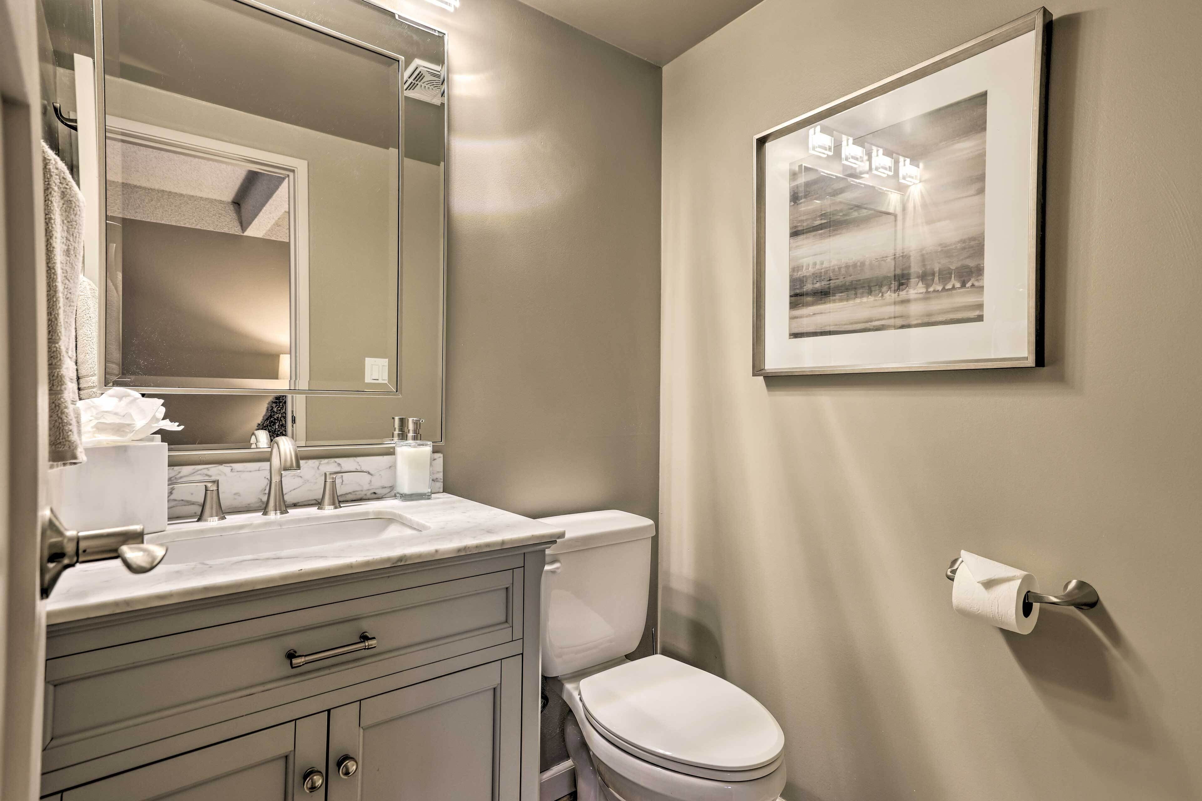 A bathroom with a sink, mirror, toilet, and a framed picture on the wall.